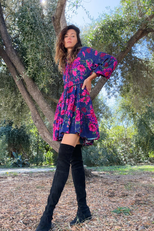 Woman in a colorful dress standing in a park with trees and greenery.